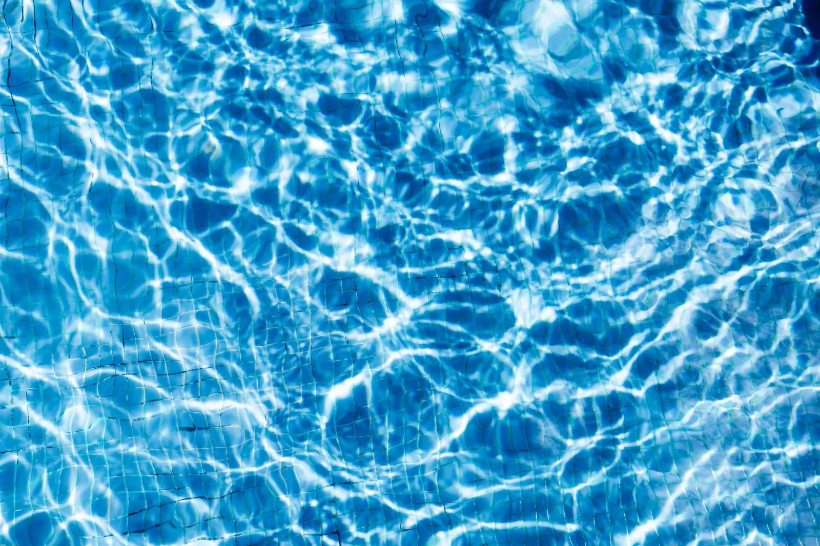 Een adembenemend abstract beeld van rimpelend blauw water dat zonlicht weerkaatst in een zwembad.