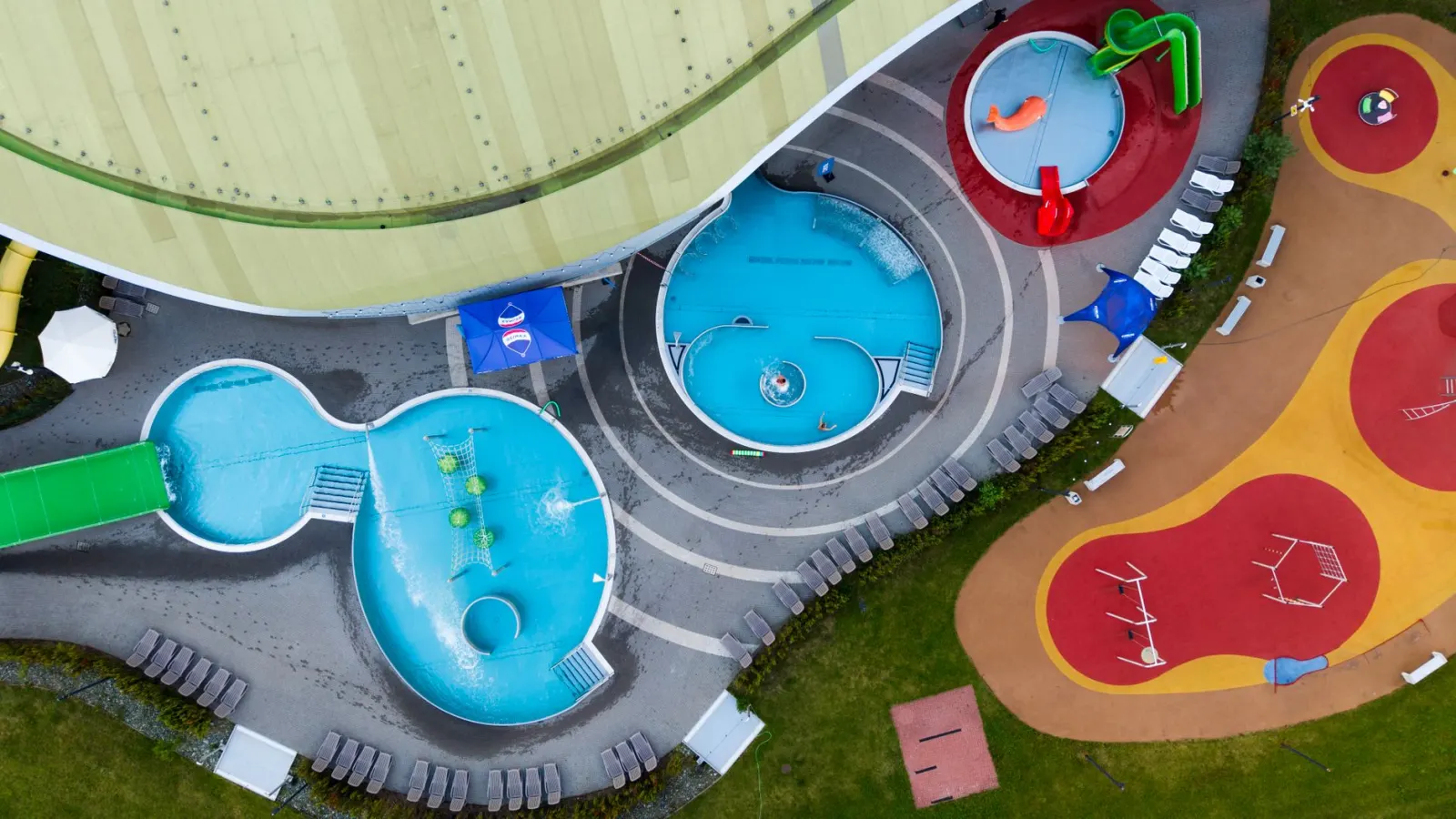 Levendige luchtfoto van een kleurrijk openluchtwaterpark met glijbanen en zwembaden.
