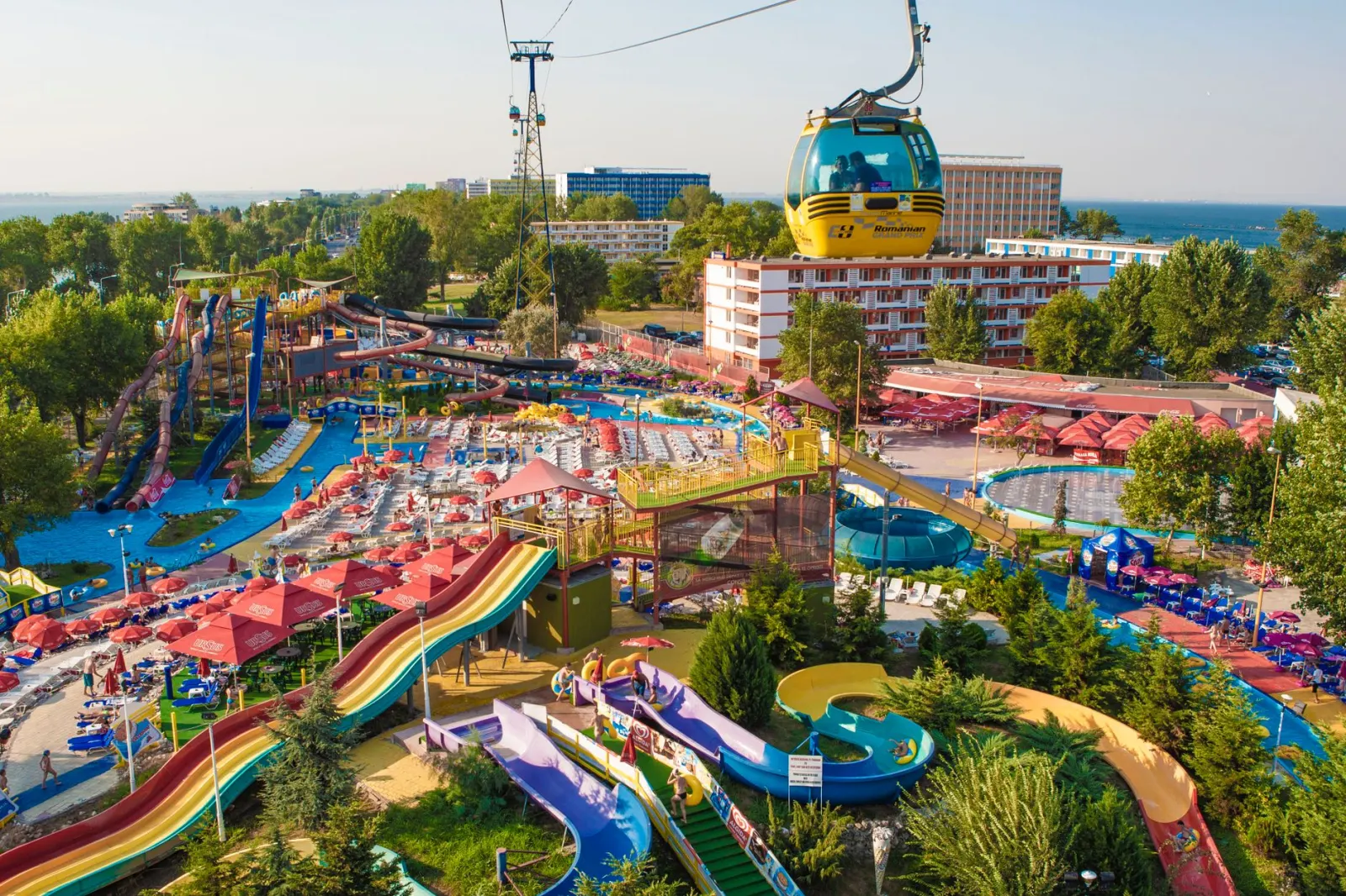 Een levendig waterpark met kleurrijke glijbanen, zwembaden en een kabelbaan onder een heldere lucht.